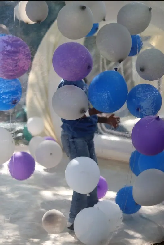 A child surrounded by purple, blue and white balloons inside a bubble house