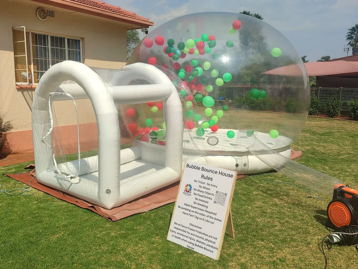 Bubble bounce house with green and red balloons on a garden lawn