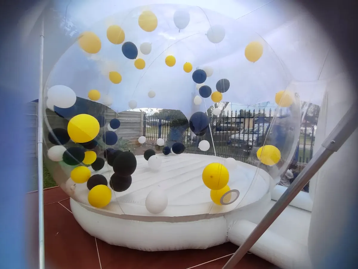Inside view of a bubble dome with yellow, black and white balloons over a white bounce cushion