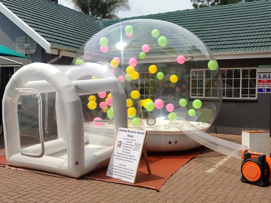 Bubble bounce house with a white bouncing cushion and colourful balloons, next to its rules board