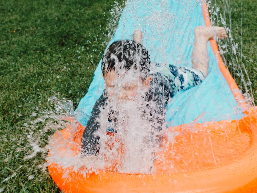 Child splashing down a blue and orange slip and slide on green grass