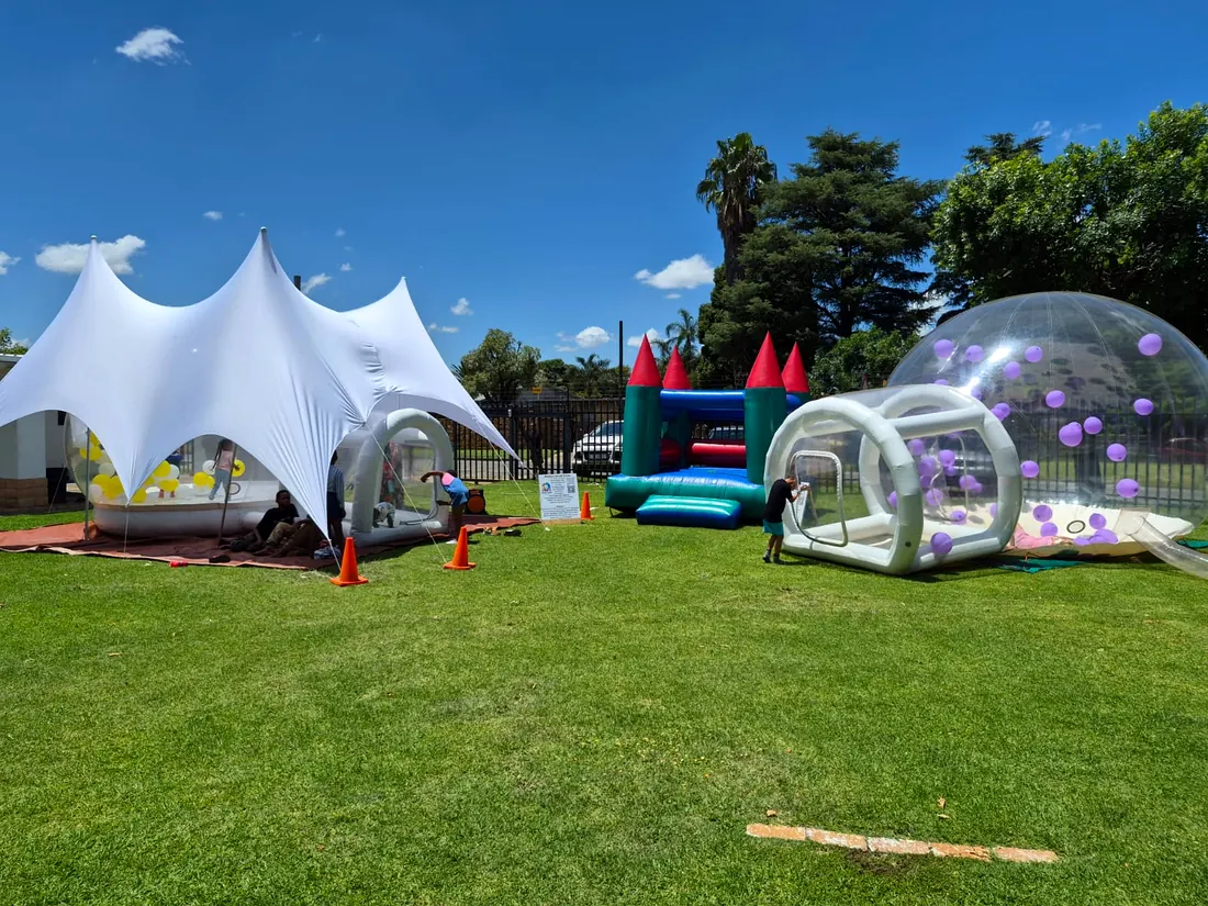 Party setup on a lawn with a white stretch tent, a jumping castle and a balloon-filled bubble dome